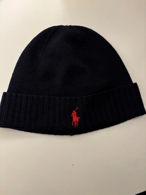 Mörk blå mössa från Polo Ralph Lauren - Mörk blå ribbstickad mössa från Polo Ralph Lauren.