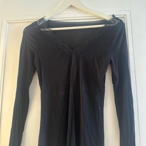 Intimissimi långärmad topp med spets - Svart långärmad topp med v-ringad hals och fina spetsdetaljer längs halsringningen och ärmsluten. Tunn och mjuk, med slim passform som sitter snyggt mot kroppen. Perfekt för dig som gillar en enkel men ändå lite extra look. Liten defekt på axeln men inga hål