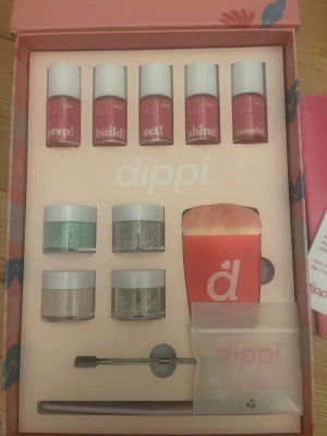 Dippi komplett nagelkit  - Nagelkit från Dippi med fem flaskor för prep, build, set, shine och nourish, samt fyra burkar powder i olika färger (mintgrön, silverglitter, lila och nude). Inkluderar en rosa borste, fil, verktyg. Extra genomskinligt pulver samt flaska med remover. Använt en enda gång. Det enda som saknas är en av två vanliga nagelfilar.  Allt levereras i en snygg rosa box med blommigt mönster. Nypris ca 1200kr. 