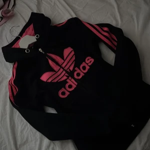 Adidas  - Svart hoodie y2k från Adidas med stor rosa logga och rosa ränder längs ärmarna. Hoodien är köpt 2016 så den är sliten 