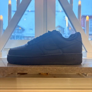 Svarta Nike Air Force 1 - Säljer ett par helsvarta Nike Air Force 1 sneakers med klassisk låg siluett. Skorna har snörning, perforerad tå och platt sula. Tillverkade i skinn med detaljer i syntet och textil på insidan. Perfekta för dig som gillar stilrena och tidlösa sneakers. Kvitto finns 🧾💞