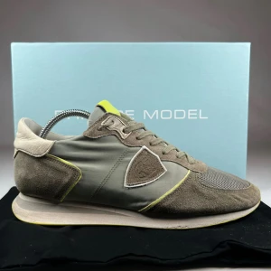 Philippe Model grå sneakers med mesh - Snygga sneakers från Philippe Model i grå och beige toner med detaljer i limegult. Ovandelen är en mix av mocka, mesh och syntet, med snörning och rund tå. Sidopanelen har en broderad sköld och sulan är platt med limegula inslag. Perfekt för dig som gillar stilrena och sportiga skor. Tillbehör: Dustbag men inte skoboxen.