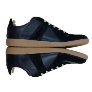 Maison Margiela svarta sneakers - Maison Margiela sneakers i svart skinn och mocka med beige snörning och gummisula. Klassisk rund tå och platt sula, med diskret logotyp på tungan. Snygg kontrast mellan svart ovandel och ljus sula, perfekt för dig som gillar stilrena och trendiga sneakers.