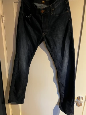 Mörkblå Lee Daren Button jeans W34 L32 - Säljer ett par mörkblå Lee Daren Button jeans med klassisk femficksdesign och snygga kontrastsömmar. Jeansen har rak passform och är tillverkade i slitstarkt denimtyg av bomull. Perfekta för dig som gillar en tidlös och clean look.