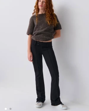 Svarta bootcut byxor med låg midja - Snygga svarta byxor med bootcut-snitt och låg midja. Byxorna har två knappar framtill och markerad söm längs benen för en cool look. Passformen är normal och materialet känns mjukt och följsamt, perfekt till sneakers eller chunky skor.❤️