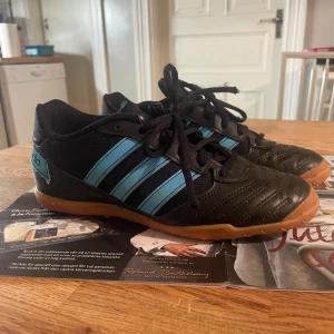 Adidas Sala svarta futsalskor  - Säljer ett par Adidas Sala fotbollsskor i svart med ljusblå ränder och detaljer. Super fin kvalité då de knappt blivit använda!