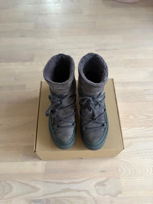 Inuikii stövlar - Säljer ett par grå/lila inuikii stövlar med mjuk päls på insidan och mocka på utsidan. Skorna har snörning med kilklack inbyggd. Perfekta nu inför vintern🤩