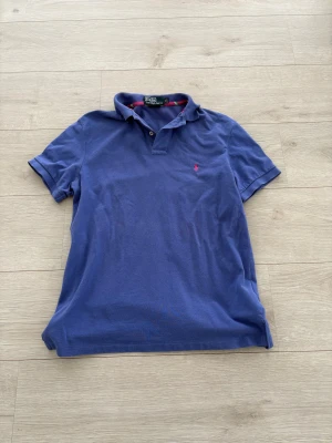 Blå piké från Polo Ralph Lauren - Blå pikétröja från Polo Ralph Lauren i storlek M. Klassisk krage, två knappar. En liten defekt på tröjan på sista bilden annars jätte fin. 
