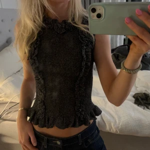 Glittrig volangtopp från Zara - Supersnygg glittrig svart topp från Zara med volangdetaljer längs sidorna och nederkanten. Toppen är ärmlös och har en ribbad struktur. Perfekt till nyår!! Storlek M men passar xs och s