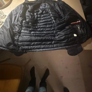 Mörkblå dunjacka Tommy Hilfiger M - Säljer en mörkblå dunjacka från Tommy Hilfiger i storlek M. Jackan har quiltad design med horisontella sömmar och klassisk Hilfiger-logga på insidan. Materialet är dun och fjäder, vilket gör den lätt och varm. Perfekt för kyliga dagar.