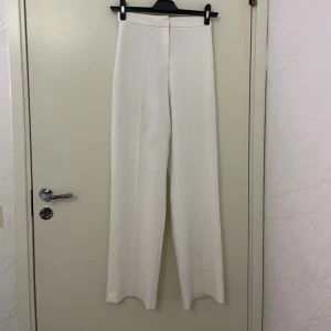 Vita wide kostymbyxor - Snygga vita kostymbyxor från H&M med rak och vid passform. Byxorna har hög midja och stilren design utan synliga fickor eller detaljer. Perfekta för en clean och modern look. Materialet känns mjukt och har ett lätt fall. Är i storlek 34 men skulle mer passa 36.
