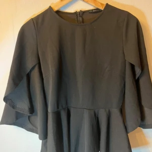 Svart topp med volangärm från SHEIN - Svart topp från SHEIN med rund halsringning och volangärmar som ger en cool och flowy vibe. Toppen har en markerad midja och dragkedja i ryggen. Perfekt för dig som gillar enkel men snygg stil. Strl S