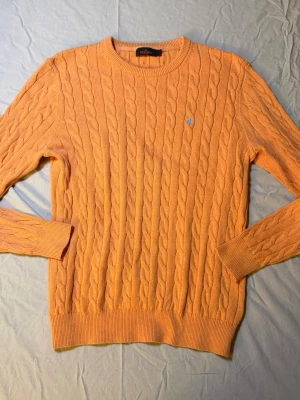 Orange kabelstickad tröja från Morris - Morris kabelstickad tröja orange – Strl L – Nyskick  Sjukt snygg orange kabelstickad tröja från Morris, storlek L, i nyskick. Riktigt fin kvalitet och färg som ger liv till outfiten utan att bli för mycket.  Perfekt för preppy, clean eller laidback stil. Funkar lika bra till jeans som chinos och under jacka eller kavaj.  Mått: Undersida: 38 cm Längd: 68 cm  • Märke: Morris • Färg: Orange • Storlek: L • Skick: Nyskick  Morris 1