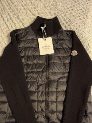 Moncler jacka - Säljer en svart jacka från Moncler. sopren design. Jackan har dragkedja framtill och Moncler-logga på ärmen. Perfekt för dig som vill ha en clean och modern look. Finns i svart och mörk blå