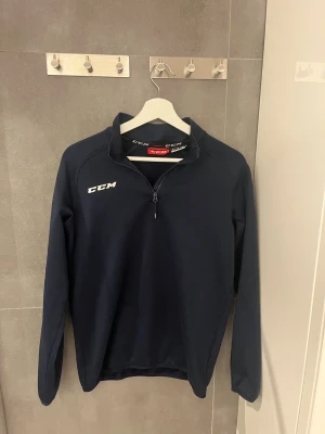 Mörkblå CCM half zip tröja  - Säljer en mörkblå långärmad tröja från CCM i storlek XL mostsvar 160cm. Tröjan har en clean look med vit CCM-logga på bröstet och praktisk half zip framtill. Perfekt för dig som gillar sportig stil och vill ha något bekvämt och funktionellt. Nypris 599kr säljs för 350kr!