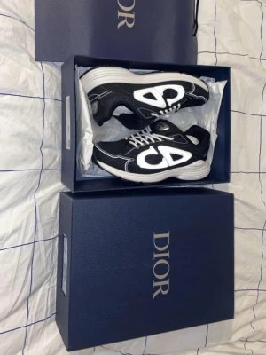 Dior B30 svarta och vita sneakers - Säljer ett par Äkta Dior B30 sneakers i svart och vitt med tydliga reflekterande detaljer och stora Dior-loggor på sidorna. Skorna har snörning, rund tå och en chunky vit sula. Ovandelen är i mesh och syntet med snygga kontrasterande sömmar. Perfekta för dig som gillar lyxiga statement sneakers. Pris kan diskuteras😄