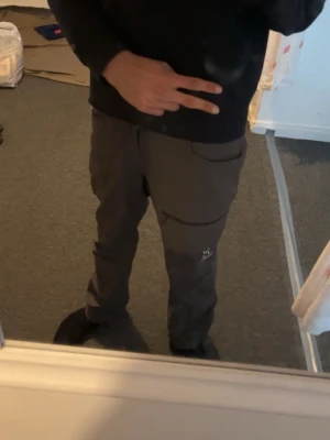 Mörkgrå cargopants från Haglöfs - Säljer ett par mörkgrå cargopants från Haglöfs med praktiska fickor och dragkedjedetalj på låret. Byxorna har en avslappnad passform och är perfekta för dig som gillar outdoor eller streetwear. Materialet känns slitstarkt och bekvämt.