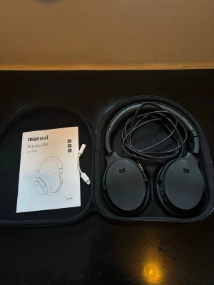 Roxcore ANC Over-Ear Hörlurar - Roxcore ANC over-ear hörlurar med aktiv brusreducering, kabelanslutning och medföljande hårt fodral. Komplett med manual och adapter. Hörlurarna ser ut att vara i gott skick utan synligt slitage. Perfekt för musik och resor.