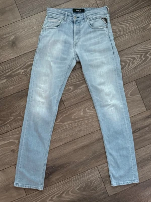 Replay Grover  - Säljer ett par ljusblå jeans från Replay med klassisk femficksdesign och snygga slitningar. Modellen är Grover. Märkesdetaljer syns på fickan och bak på linningen.