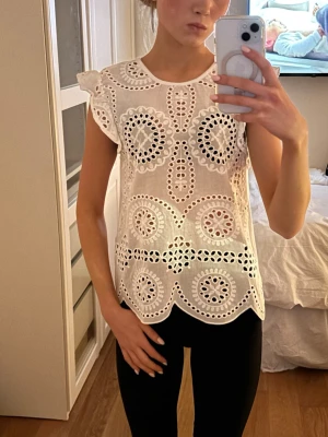 Vit broderad blus med volagärm  - Assnygg vit topp med spets/ mönster. Köpt i somras men aldrig använd!! Prislappen sitter kvar på tröjan. Säljer eftersom att den inte har kommit till användning mycket alls. Storlek XS/S!