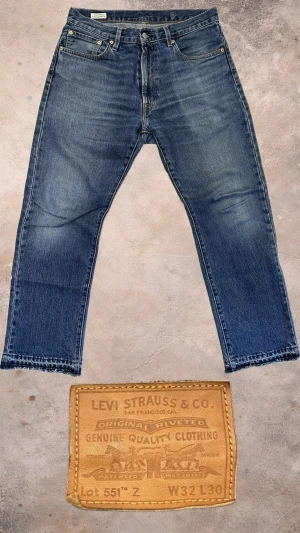 Levi's 551Z blå jeans W32 L30 - Klassiska Levi's 551Z jeans i blå tvätt med raka ben och femficksmodell. Jeansen har en snygg vintage look med slitningar och kontrastsömmar. Tillverkade i robust denim med läderpatch bak och röd Levi's-tagg på bakfickan. Perfekta för en avslappnad stil.