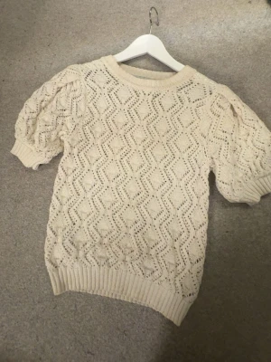 Beige stickad topp med puffärm - Supersöt beige stickad topp med kort puffärm och ribbade muddar. Perfekt till både jeans och kjol för en chill look.