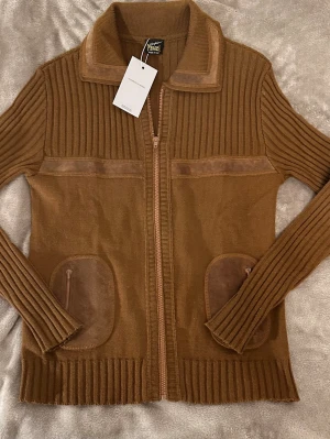 Stickad cardigan jacka - Sällsynt vintage italiensktillverkad dragkedjekofta/stickad jacka från Confezioni Perica. Tillverkad av högkvalitativ ribbad ullstickning med äkta mockapaneldetaljer över bröstet, kragen och fickorna. Ett vackert strukturerat plagg som bärs mer som en lätt jacka än en tröja.  Såld i Confezioni Perica affärer på 70-90 talet för 3500-4000kr Skulle säga 8,5-9/10 skick.