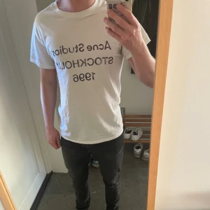 Vit t-shirt från Acne Studios - Vit t-shirt från Acne Studios med svart tryck 'Acne Studios Stockholm 1996' på bröstet. Klassisk passform och rund halsringning, perfekt för en clean och stilren look. Tillverkad i mjuk bomull.