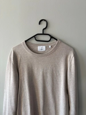 Beige stickad tröja från Bläck - En stilren beige stickad tröja från Bläck i storlek S. Tröjan har rund halsringning, ribbade muddar och lång ärm. Perfekt för lager på lager och enkel att matcha med olika outfits.