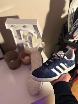 Adidas Gazelle mörkblå sneakers - Säljer ett par Adidas Gazelle sneakers i mörkblå mocka med vita detaljer. orginal pris ligger på 1200 och säljs rätt biligt