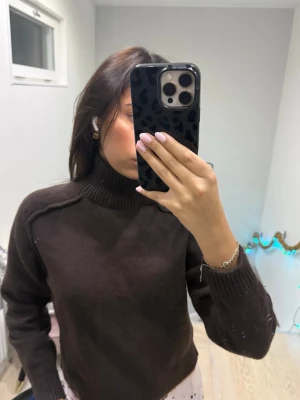 Brun polotröja i stickat material - Mysig brun polotröja i stickat material med ribbad krage och muddar. Tröjan har en klassisk passform och är perfekt för kyliga dagar. Enkel att matcha med jeans eller kjol för en chill look.