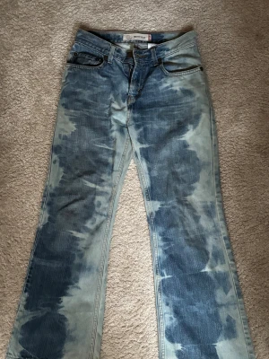 Levi's Jeans  - Säljer ett par Levi's 527 Bootcut jeans i blått med unik tie-dye effekt. Modellen har klassisk femficksdesign, låg midja och bredare benslut. Jeansen är tillverkade i 100% bomull och har råa kanter längst ner för en edgy vibe. Såå sjukt coola!! Bra skick förutom längst ner där de saknas några stygn💙