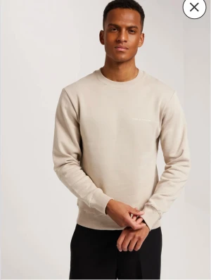 Beige sweatshirt från Tiger of Sweden - Säljer en stilren beige sweatshirt från Tiger of Sweden med diskret logga på bröstet. Tröjan har rund hals, ribbade muddar och är långärmad. Perfekt för dig som gillar en clean och enkel look.