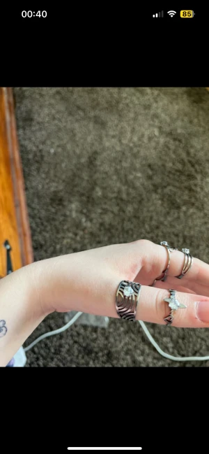 Set med sex silverfärgade ringar - Säljer ett set med sex snygga ringar i silverfärg. Ringarna har olika former och detaljer, bland annat vågiga mönster, hjärtformad design och glittrande stenar. Perfekt för dig som gillar att mixa och matcha flera ringar på samma hand.