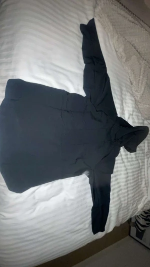 Svart Nike vindjacka med huva - Svart vindjacka från Nike med huva och hel dragkedja framtill. Jackan har en stilren design, två sidofickor och är tillverkad i lätt polyester som passar perfekt för blåsiga dagar. Snygg och enkel att matcha med streetwear eller sportiga outfits. Den är helt oanvänd 