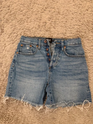 Blå denimshorts   -  blå jeansshorts från lager 157 med hög midja. Shortsen har knappar framtill och rå, fransig kant nedtill. Tillverkade i bomull.