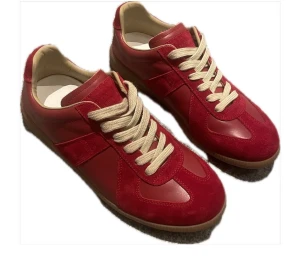 Röda Maison Margiela - Maison Margiela sneakers i rött skinn och mocka med beige snörning och gummisula. Klassisk rund tå och platt sula, snygg retrostil med kontrasterande material. Perfekt för dig som gillar statement-färgade skor och vill sticka ut. 