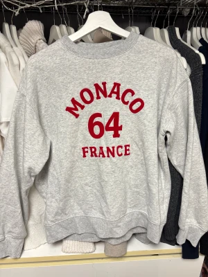 Grå sweatshirt från H&M - Snygg grå sweatshirt med tryck i rött där det står MONACO 64 FRANCE på framsidan. 