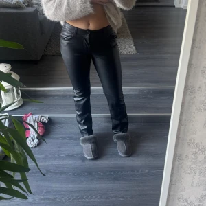 Svarta skinnbyxor med raka ben - Snygga svarta byxor i skinnimitation med raka ben och klassisk femficksdesign. Byxorna har låg midja och stängs med knapp och dragkedja, insidan är mjuk så dem värmer lite extra nu till höst och vinter! Använda max 2 gånger så i bra skick ! 