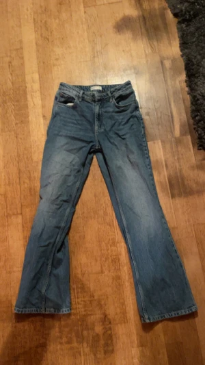 Blå jeans med bootcut - Säljer ett par klassiska blå jeans med bootcut och normal passform. Jeansen har fem fickor, dragkedja och knapp framtill. Perfekt för dig som gillar en avslappnad stil med lite vidare ben. Materialet är slitstarkt denim.