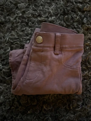 Plommonlila byxor med ribbade detaljer KappAhl - Snygga lila byxor från KappAhl i storlek 116. De har ribbade detaljer på benen och klassisk femficksdesign med knapp framtill. Materialet är mjukt och stretchigt, perfekt för dig som gillar bekväma och coola plagg.