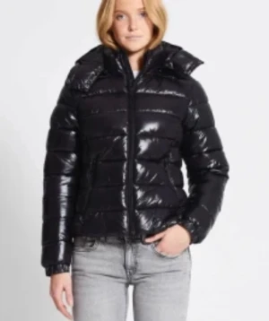 Svart glansig pufferjacka med dragkedja - Snygg svart pufferjacka med glansig finish och hög krage. Jackan har horisontella quiltade partier och praktisk dragkedja framtill. Perfekt för dig som vill ha en cool och varm look under kalla dagar. Aldrig använd helt ny.