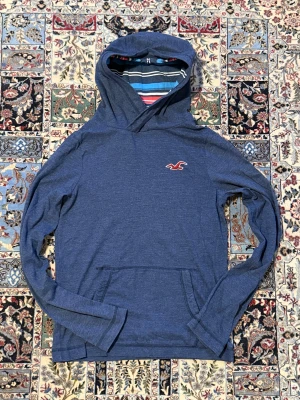 Hollister Hoodie – Strl S - Mysig och stilren hoodie från Hollister i blåmelerad färg. Randigt foder i huvan som ger en fräsch och unik look. Perfekt till vardag, höst och vinter.  Passform: Storlek S och sitter perfekt på mig som är 176 cm och väger 73 kg. Modellen är mer åt det slimmade hållet, så den är bäst för dig som vanligtvis använder S.  Skick: 9/10 Väldigt fint skick utan skador eller slitage.  Hör av er vid frågor så kan jag skicka fler bilder eller mått.
