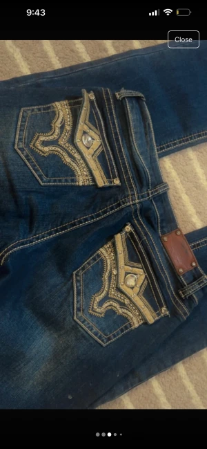 Stars & Stripes blå jeans med broderi - Mörkblå jeans från Stars & Stripes med snygga broderade bakfickor i guld och silvertråd samt dekorstenar. Klassisk femficksmodell med flared ben och kontrastsömmar. Jeansen har normal passform och är tillverkade i jeansmaterial.