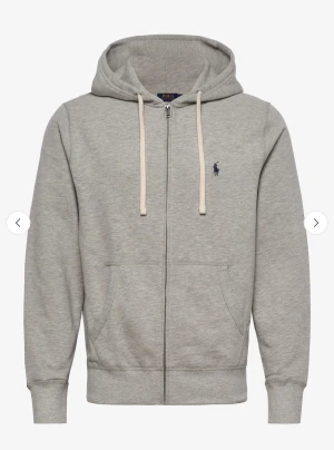  Polo Ralph Lauren Grå hoodie - Grå hoodie från Polo Ralph Lauren med dragkedja och huva med vita snören. Klassisk broderad logga i mörkblått på bröstet. Tröjan har två fickor framtill och ribbade muddar vid ärmslut och nederkant. Storlek M. Använd men i gott skick