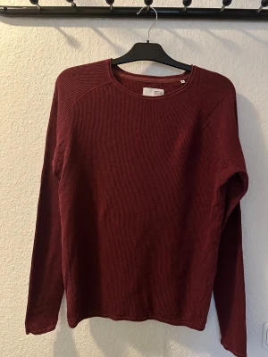 Vinröd stickad tröja från Solid - Vinröd stickad tröja från Solid i storlek M. Tröjan har rund halsringning och är tillverkad i ett grovstickat material som ger en chill och avslappnad vibe. Perfekt för dig som gillar enkel och stilren design med lite struktur.