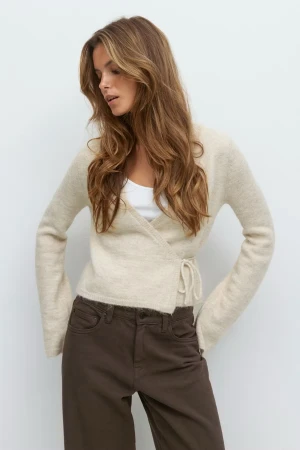 Beige omlottkofta från Gina Tricot - Säljer en beige omlottkofta från Gina Tricot med knyt i sidan. Koftan är croppad, har lång ärm och är stickad i mjukt material som känns skönt mot huden. Perfekt att slänga på över ett linne för en chill look.