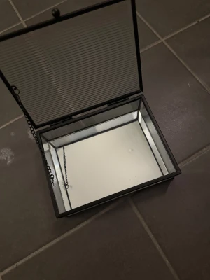 Svart och transparent boxväska i glas - Säljer en stilren boxväska i glas med svarta metallkanter och kedjedetalj. Väskan har rektangulär form, ribbat glas på sidor och lock samt spegelbotten för extra cool effekt. Perfekt för dig som gillar unika accessoarer med modern vibe. Kom med bud! Nypris 1200kr