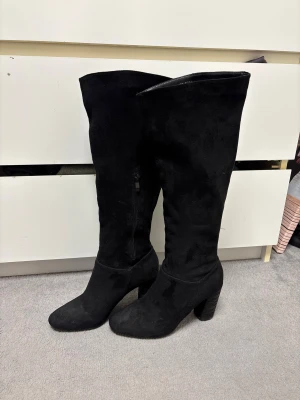 Svarta höga mockastövlar med klack - Snygga svarta stövlar i mocka. Stövlarna är knähöga och har dragkedja på insidan för enkel på- och avtagning. Använda 2 utgångar