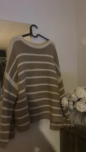 Randig beige stickad tröja - Säljer en oversized stickad tröja med breda beige och vita ränder. Tröjan har rund hals och långa ärmar, perfekt för dig som gillar chill och comfy stil. Materialet är grovstickat och ger en mysig känsla. Passar dig som gillar neutrala färger och relaxed vibe.